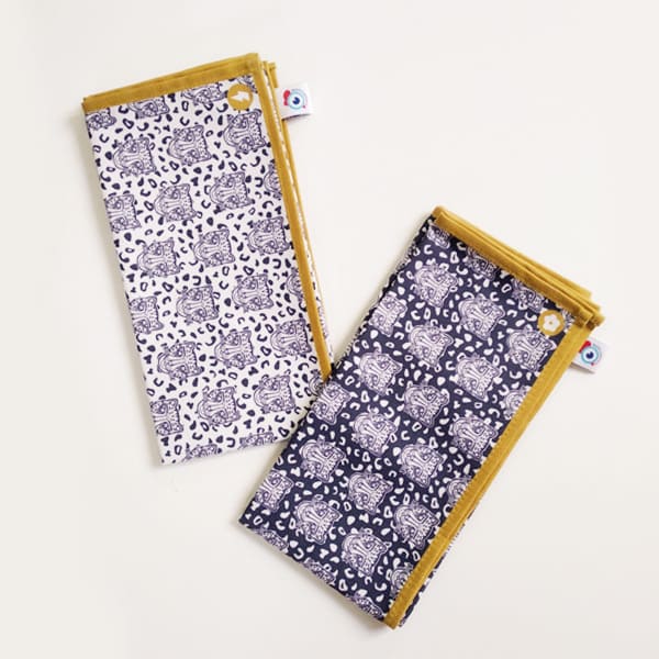 Lot de 2 serviettes de table en tissu, famille déco Grrr, motif léopard fond naturel et motif léopard fond bleu foncé. Bord ocre